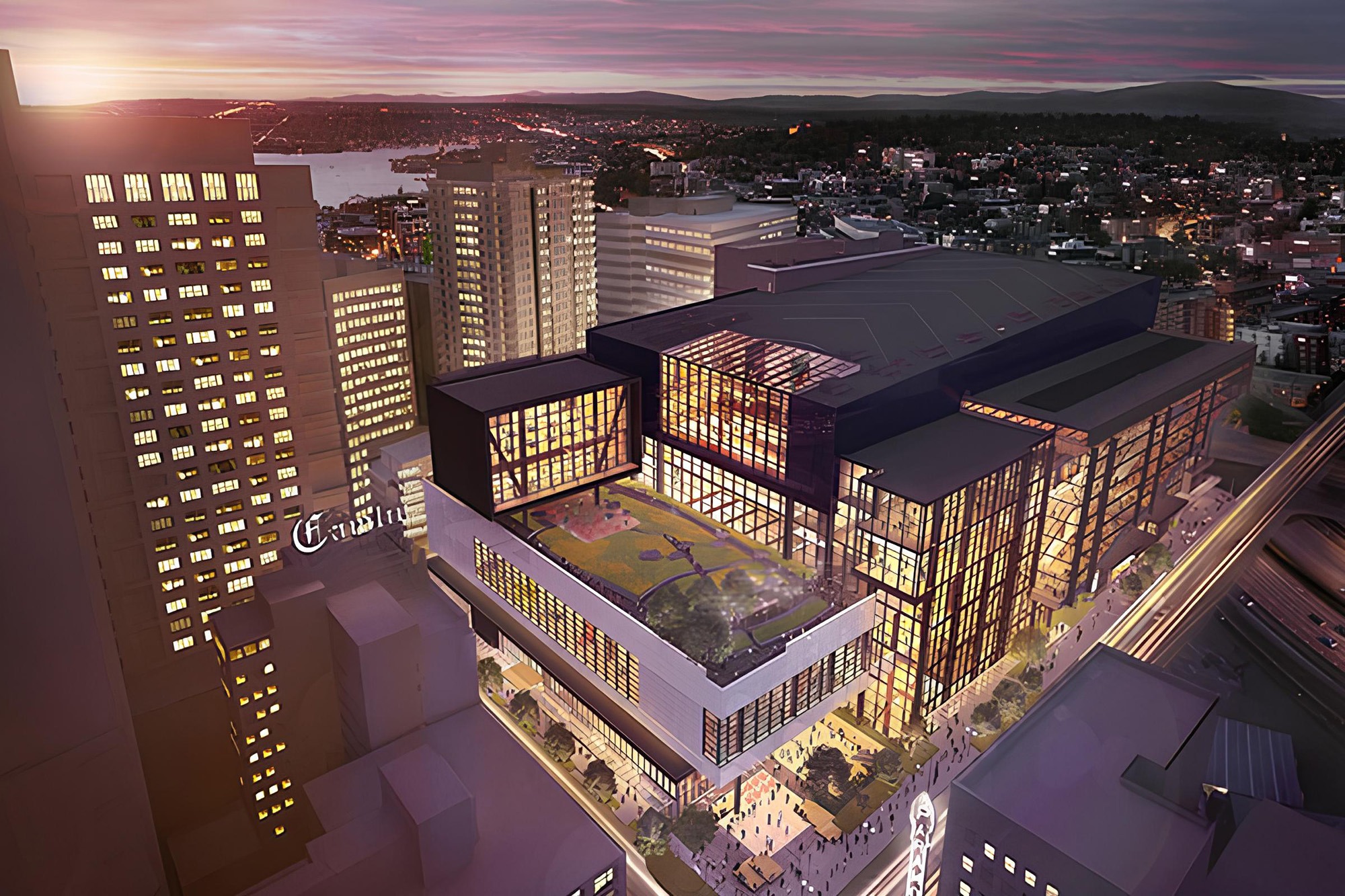 Aerial view of a modern multi-story building with a rooftop garden, surrounded by city skyscrapers, showcasing urban development and evening lighting.