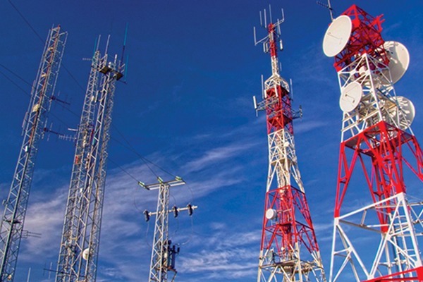 Telecommunications towers of various heights and designs against a blue sky. These structures facilitate mobile and internet connectivity.