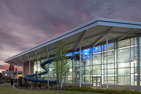 Modern recreational center featuring a large glass facade and a blue water slide, set against a vibrant sunset sky. Ideal for family activities.