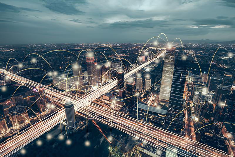 Aerial view of a bustling urban landscape at night, showcasing illuminated skyscrapers and busy highways, overlaid with digital connectivity lines.
