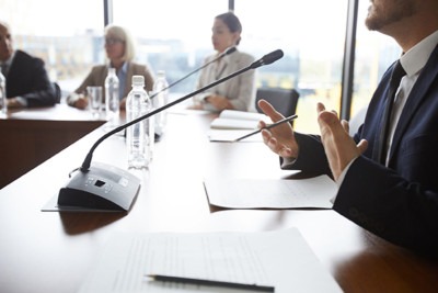 A professional meeting in a modern conference room, featuring a speaker gesturing while discussing points with colleagues.