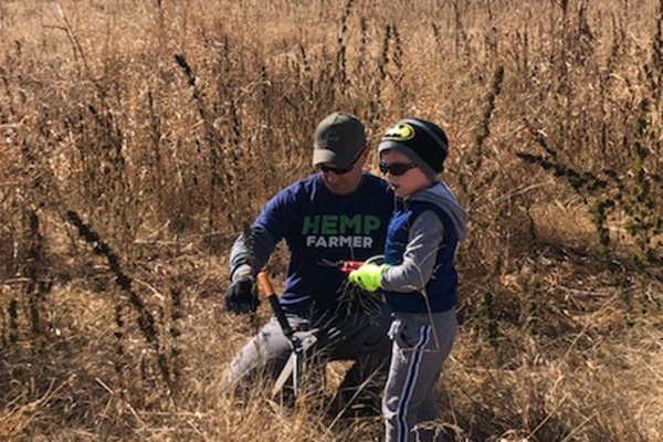 A man and a young boy are engaged in farming activities in a field, with the man holding a tool. The boy watches intently, showcasing a hands-on learning experience.
