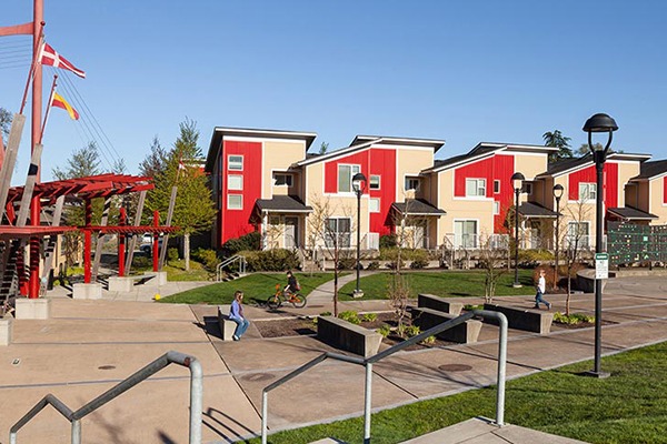 Colorful residential complex features beige and red townhouses, landscaped pathways, and recreational areas with people engaging in activities.