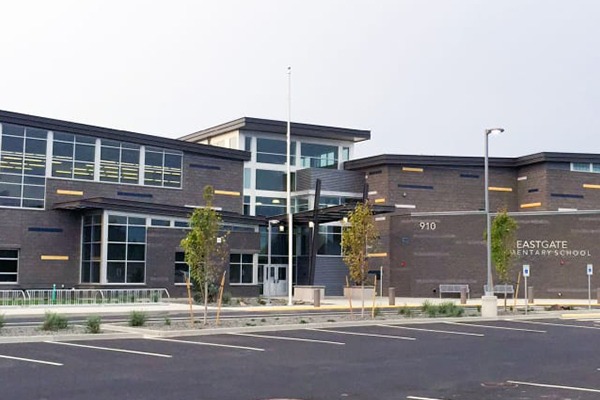 Modern school exterior features a mix of brick and glass, with a landscaped entrance and nearby parking area.