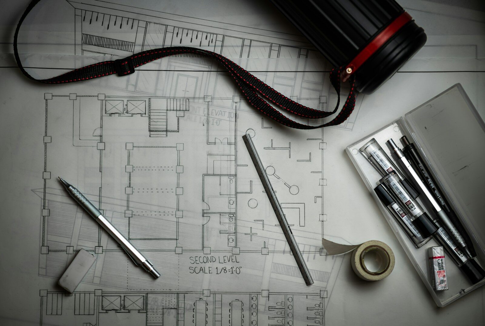 Architectural blueprints with drafting pencils, a metal ruler, and a storage tube
